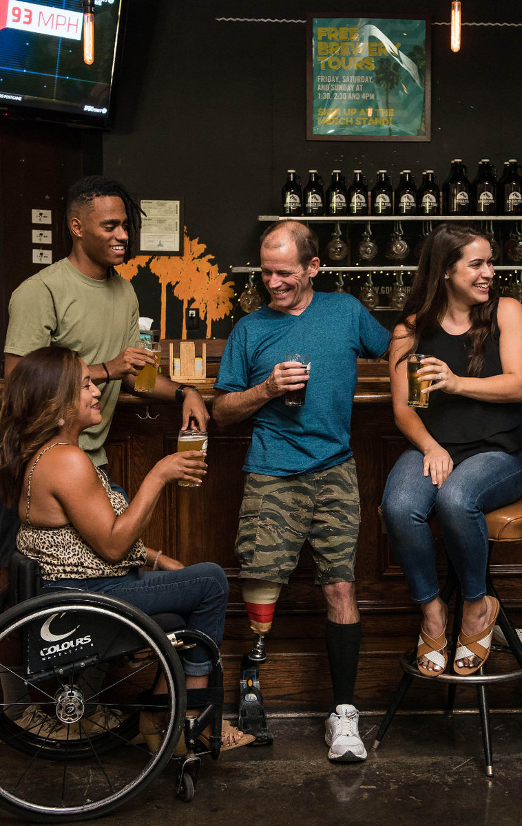 A group of friends gather at a bar, one of them is in a wheenchair and another has a prosthetic leg.